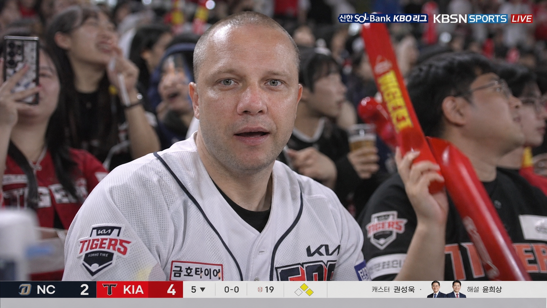 AI baseball fan cam trend example showing the subject seated in a KBO Korean baseball stadium with live broadcast scoreboard graphics