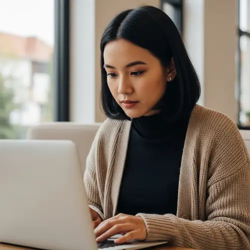 Focused Asian Freelance Worker Using Laptop in Coffee Shop