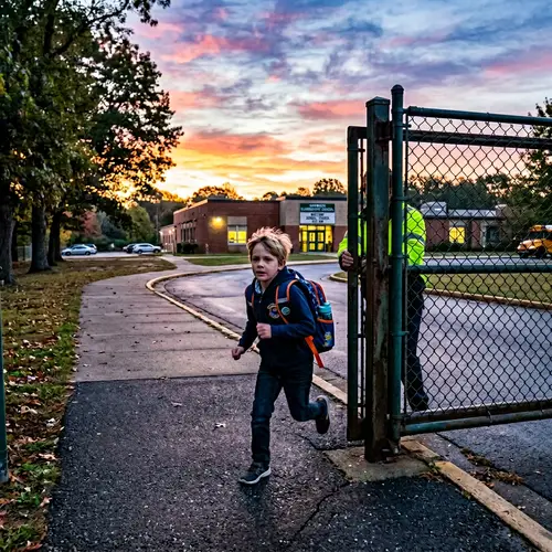 Suburban School Scene at Dawn: Caucasian Boy Rushing Through Gate
