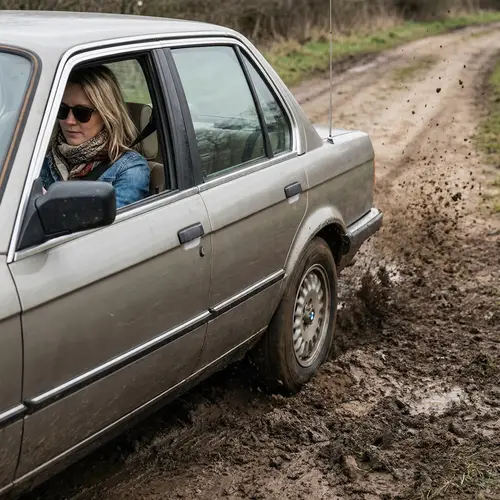 Trendy Woman in Aged BMW Spinning Tires in Mud