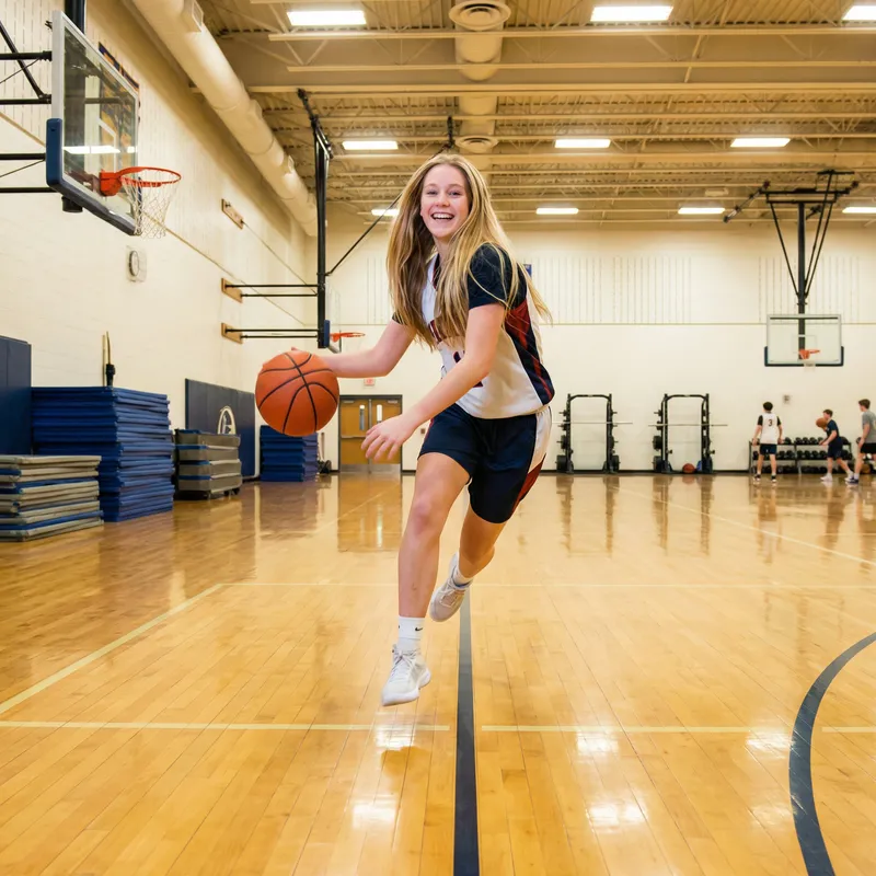 Smiling Blonde Girl Playing Basketball in Gym