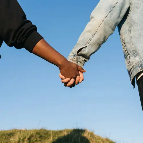 Interracial Couple Holding Hands Against Clear Blue Skies