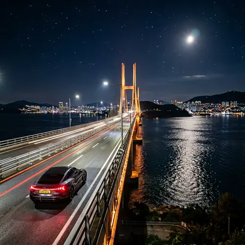 Luxury Electric Car Driving on Moonlit Bridge Over Sea Strait