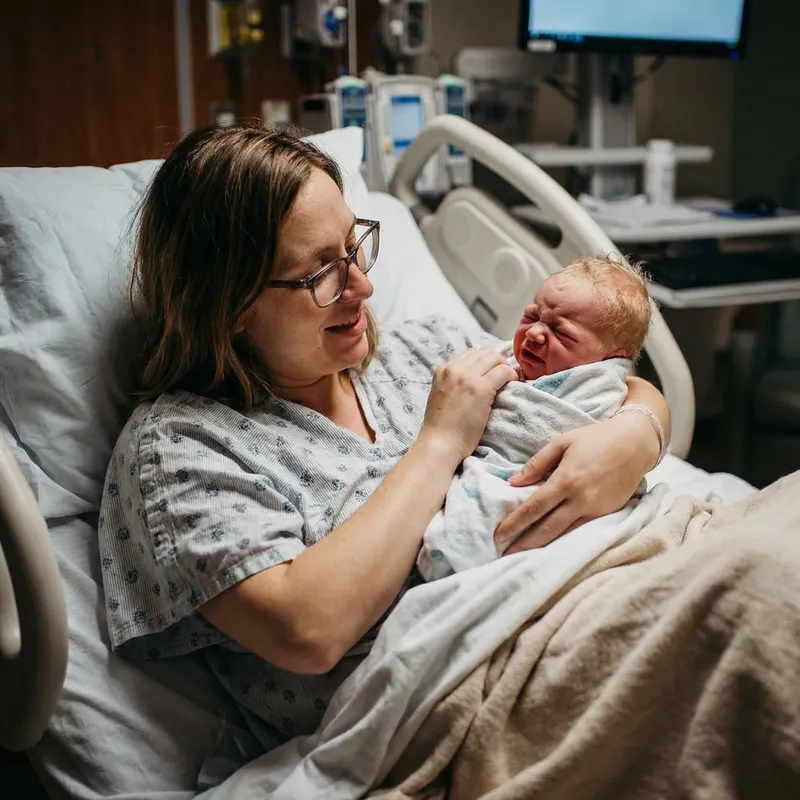 Caucasian Mother with Bangs Holds Crying Newborn in Hospital