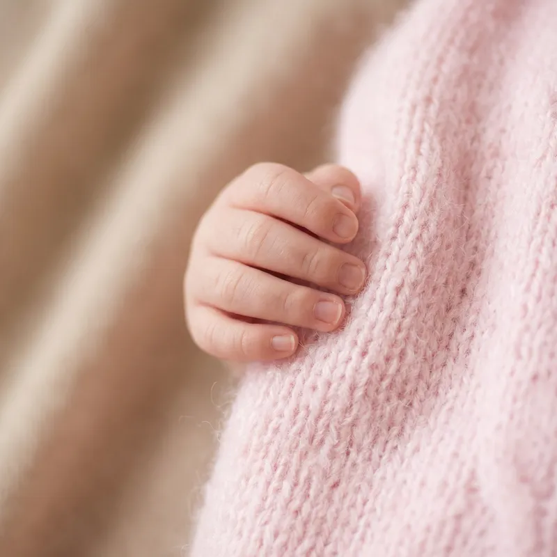 Delicate Newborn Baby Hand in Pink Clothing on Soft Beige Background