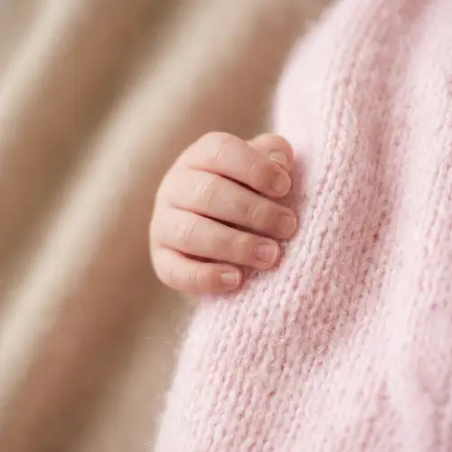 Newborn Baby Hand in Pastel Pink Clothing on Beige Background