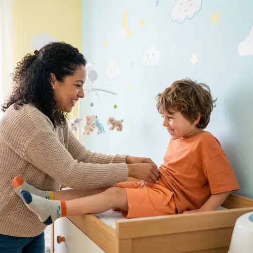 7-Year-Old Boy in Orange Shirt and Diaper Getting Help from Mom