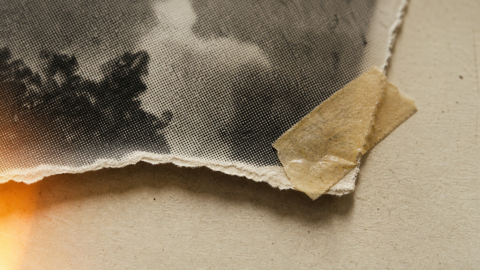Close-up of Vox-style analog textures: halftone-printed photo with a torn paper edge and aged tape on grainy cream paper with a warm light leak
