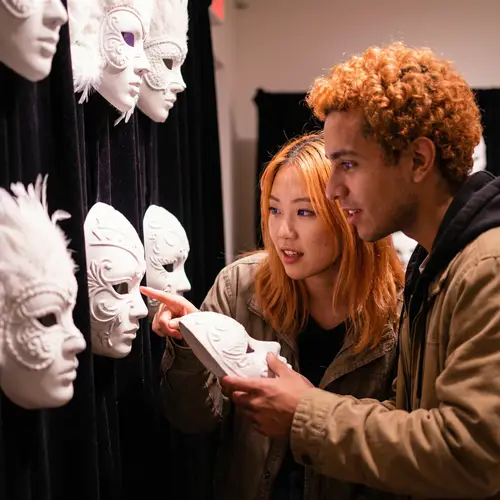 Young Adult Asian Woman & Hispanic Man Choosing Intricate White Masks
