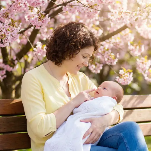 Tender Moment: Mother Cradling Newborn Baby Under Cherry Tree